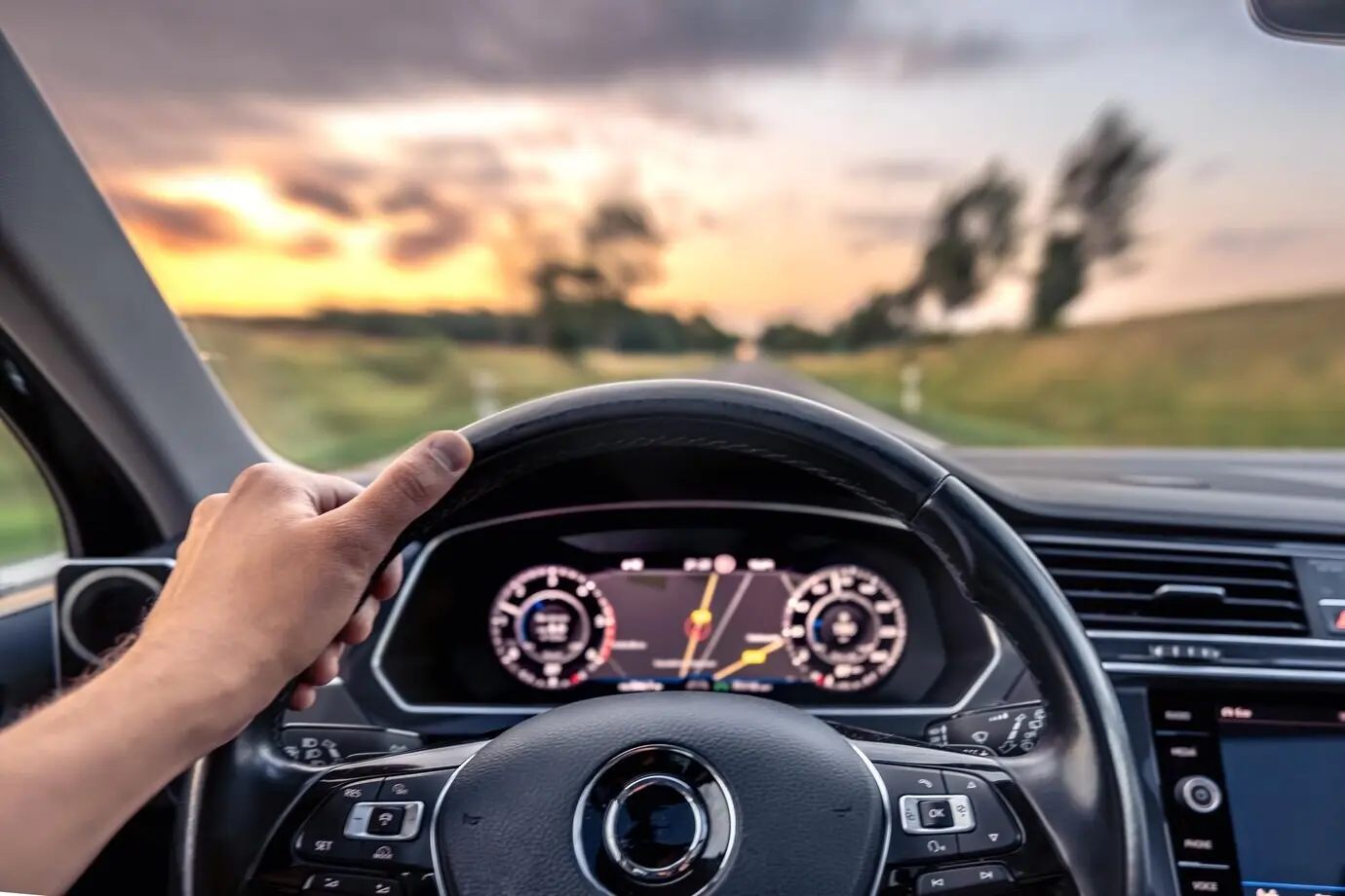 Hand am Lenkrad, während der Fahrt, Roadtrip bei Sonnenuntergang.